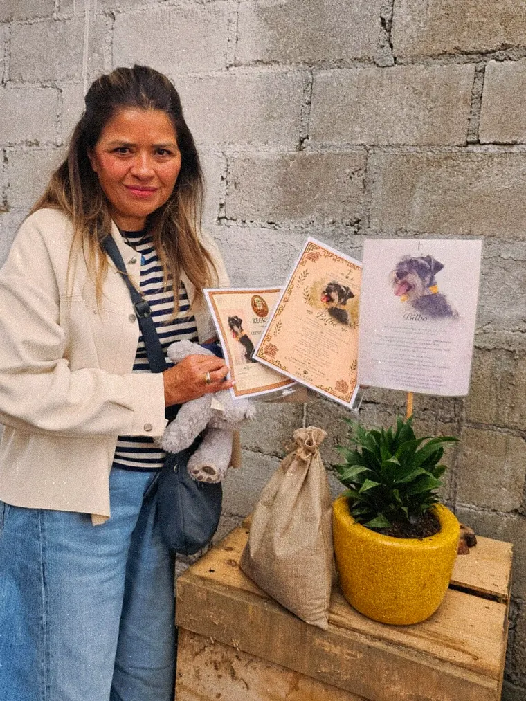 Una mujer sonríe en el compostario junto a su certificado, una planta en maceta amarilla y un costalito de yute
