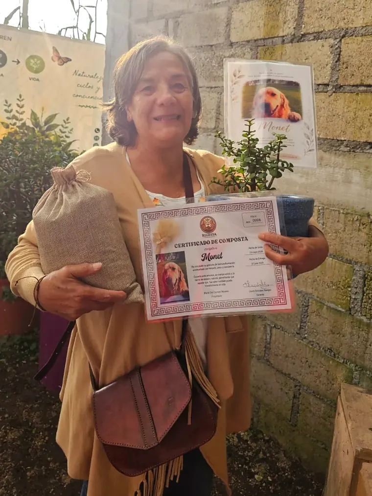 Una señora sonríe mientras sostiene el certificado de Monet y su costalito de yute